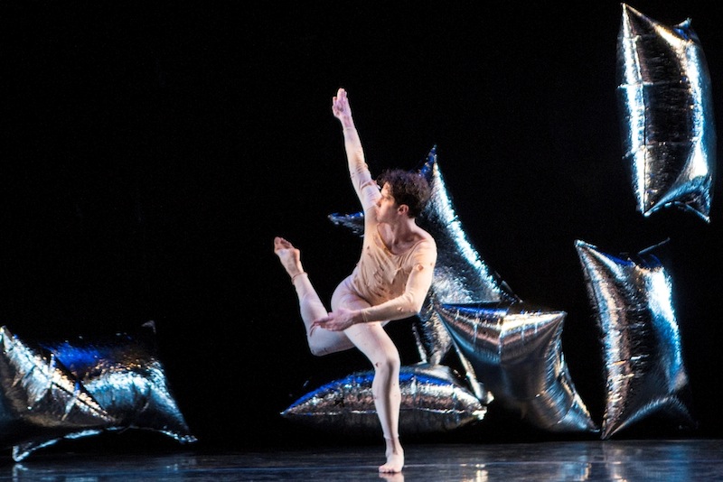 Joshua Tuason in RainForest. Tuason executes a one footed balance in attitude position. He looks at his hand, reaching for the sky